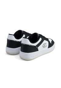 Schwarz-weiße Sneaker verfügen über ein glattes synthetisches Obermaterial, eine Schnürung, eine Gummisohle und ein kontrastierendes Logo an der Ferse und an der Seite.