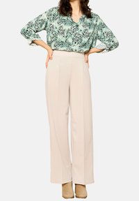 Zelená vzorovaná blůza s výstřihem do V, spárovaná s béžovými kalhotami s vysokým pasem. Tkanina je měkká a hladká; kalhoty mají skladby.