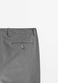 Vue arrière d'un pantalon de costume gris montrant des passants de ceinture et une poche arrière à bouton unique avec une petite étiquette métallique.