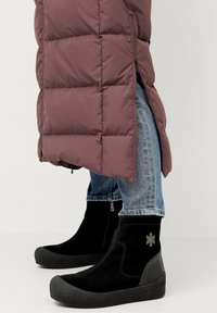 Lila Daunenjacke mit gestepptem Design, kombiniert mit blauen Jeans und schwarzen Stiefeletten mit strukturiertem Sohlen und silbernem Akzent.