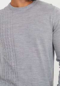 Szary sweter z dzianiny z okrągłym dekoltem i wzorem w warkocze po lewej stronie. Miękka tekstura z długimi rękawami.