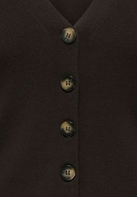 Dunkelbraune Strickjacke mit V-Ausschnitt und fünf runden, glatten Knöpfen mit dezentem Glanz und zwei Löchern. Gerippte Struktur.