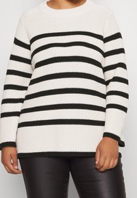 Pull en maille avec de larges rayures noires et blanches, encolure ras du cou et manches longues avec des poignets côtelés. Tissu texturé et coupe décontractée.