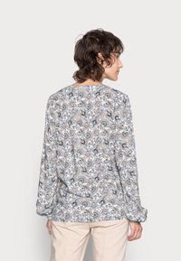 Blusa de mangas longas em tecido leve, com um padrão floral em tons de azul, preto e pêssego, com decote redondo e corte descontraído.