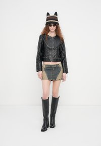 Μαύρο δερμάτινο κοντό μπουφάν με ασημένια καρφιά, ελιάς και μπλε φτιαγμένη από διαφορετικά κομμάτια τζιν μίνι φούστα, μαύρες μπότες μέχρι το γόνατο και ριγέ πλεκτό σκουφάκι.