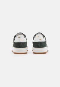 Green suede sneakers with white leather accents, rubber outsoles, and subtle gold branding on the heel. Minimalist design, clean lines.