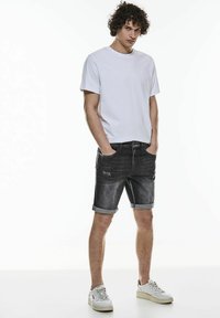 Valkoinen pyöreä kaula-aukkoinen t-paita, joka on yhdistetty tummanharmaisiin farkkushortseihin, joissa on käännetyt lahkeet ja hieman kulunut ilme, sekä taskut. Asusteena valkoiset tennisliuskat.