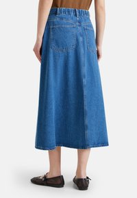 Džínová sukně s volným střihem, elastickým pasem a dvěma zadními kapsami. Má střední délku a světle modrou barvu.