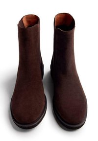 Botas de ante marrón hasta el tobillo con un diseño sencillo, punta redondeada y aberturas laterales minimalistas. Suelas de goma negra con dibujo texturizado.