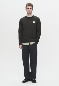 Dark knit sweater with round neckline featuring a white letter "W" logo, layered over a green and white striped shirt, paired with black trousers.