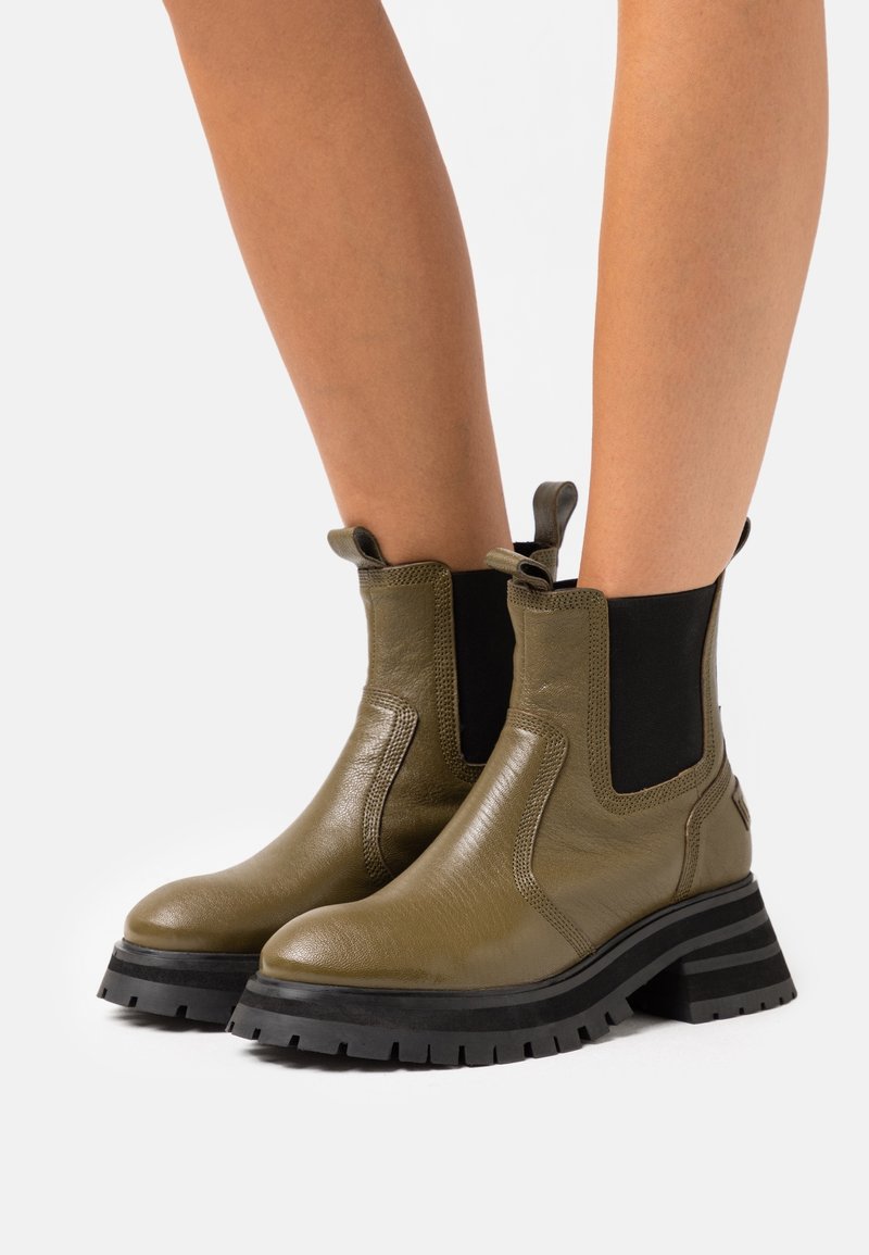Bottes cheville en cuir vert olive avec panneaux élastiques et languettes de tirage ; semelle épaisse en caoutchouc noir avec rainures ; texture lisse et bout arrondi.