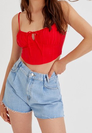 Mujer con una camiseta corta roja con detalle de lazo y shorts vaqueros azul claro de cintura alta con dobladillos deshilachados.