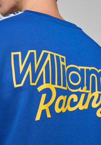 Niebieska bawełniana koszulka z żółtym napisem "Williams Racing". Posiada okrągły dekolt i gładką teksturę, z kontrastującymi akcentami na ramionach.