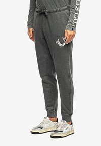 Grijze joggingsbroek met een elastische tailleband en trekkoord, zijzakken en een bedrukte logo op de linker bovenbeen. Textuurstof met een relaxte pasvorm.