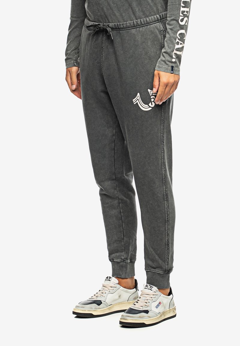 Grijze joggingsbroek met een elastische tailleband en trekkoord, zijzakken en een bedrukte logo op de linker bovenbeen. Textuurstof met een relaxte pasvorm.