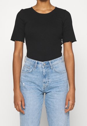 Personne portant un haut noir ajusté à manches courtes avec des bords ondulés en forme de laitue et un jean en denim bleu clair taille haute.