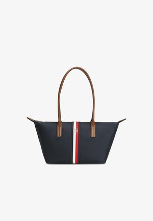 Sac cabas bleu marine avec anses marron et détail central rayé rouge, blanc et bleu marine avec petit logo doré sur le devant.