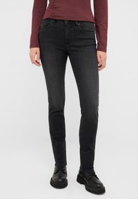 Czarne dżinsy o slim fit, z pięcioma kieszeniami, szlufkami na pasek i subtelnym efektownym wyblednięciem. Noszone z czarnymi butami z sznurowadłami.