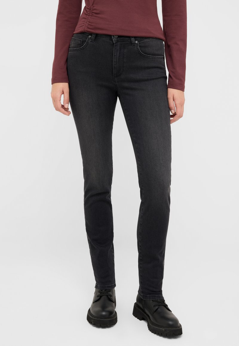 Czarne dżinsy o slim fit, z pięcioma kieszeniami, szlufkami na pasek i subtelnym efektownym wyblednięciem. Noszone z czarnymi butami z sznurowadłami.