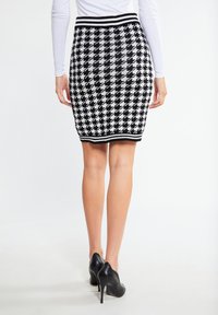 Dámská tužková sukně s černobílým vzorem houndstooth a silným černým žebrovaným pasem. Nosit s černými vysokými podpatky.
