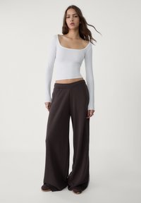 Top bianco a maniche lunghe con scollo quadrato, abbinato a pantaloni morbidi marroni con vita elasticizzata.