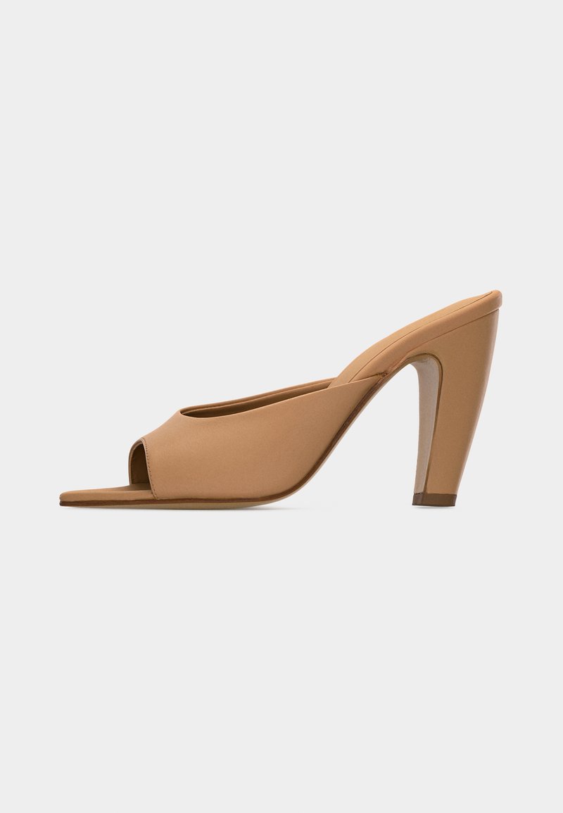 Mule beige à bout ouvert et talon haut, finition lisse et talon effilé, sur un fond clair uni.