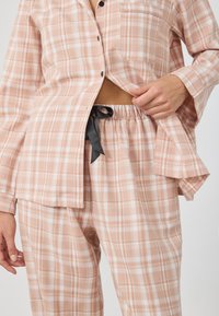 Roosa ruuduline vabaaja komplekt, mis sisaldab nööbiga särki taskuga ja sobivaid pükse elastse vöökoha ja musta stringiga.