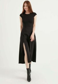 Schwarzes Maxikleid mit kurzen Ärmeln und hohem Schlitz auf der linken Seite. Glatter, dehnbarem Stoff; subtile Textur; tailliertes Oberteil.