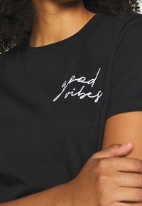 Black cotton t-shirt featuring a white handwritten "good vibes" text on the left chest area. Short sleeves and a crew neckline.