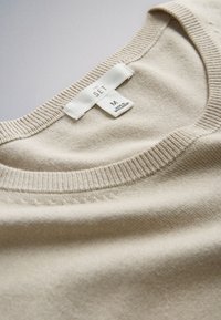 Pulover bej din tricot cu guler rotund tip ribs și o etichetă albă cu inscripția "THE SET" și mărimea medie, fabricat în Bangladesh.