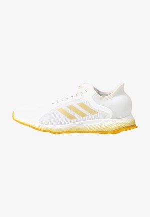 Chaussure de sport blanche avec une tige en mesh, une semelle jaune et des accents texturés. Présente trois bandes jaunes et un design de talon arrondi.