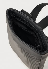 Black vertical ribbed shoulder bag with a smooth texture, zippered opening, interior compartments, and an adjustable strap.