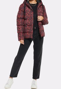 Rød og sort leopardprint puffjakke, med lynlåslukning, hætte og ensfarvet sort for. Sammen med sorte jeans og hvide sneakers.