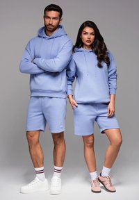 Haut à capuche bleu clair et shorts en tissu doux ; le haut à capuche possède une poche kangourou, les shorts disposent d'une taille élastique et d'un branding discret.