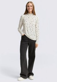 Haut à manches longues crème à pois noirs, col montant, associé à un pantalon noir à jambes larges et des baskets blanches. Texture de tissu lisse.