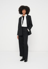 Costum negru croît cu sacou cu nasturi simplu rând, cămașă albă, cravată neagră și pantaloni largi. Material neted și ghete cu vârf ascuțit.