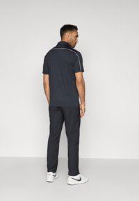 Σκούρο γκρι πόλο μπλουζάκι με κοντά μανίκια και λευκές διακοσμητικές ραφές, συνδυασμένο με ταιριαστά σκούρα παντελόνια και λευκά αθλητικά παπούτσια.