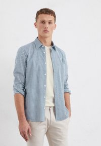 Button-up shirt in light blue with a geometric pattern. Material appears lightweight. Styled with rolled sleeves and paired with a light-colored undershirt.