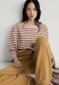 Gestreepte lange mouwen shirt in crèmekleur en roesttinten, gecombineerd met mosterdgeel, losse broek; zachte stof, relaxte pasvorm en brede mouwen.