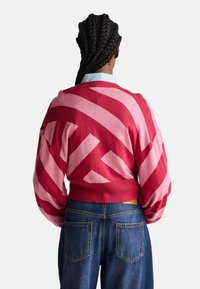 Gestreifter Pullover in Rot und Pink mit kräftigen diagonalen Streifen. Verfügt über einen gerippten Bund und eine entspannte Passform. Getragen mit hoch taillierten Jeans.