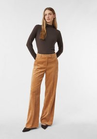 Brązowy golf z długimi rękawami, zestawiony z wysokim stanem i szerokimi nogawkami spodni sztruksowych w ciepłym beige odcieniu.