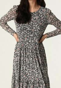 Vestido floral con base negra, con patrones de flores blancas y rojas, mangas largas transparentes, escote redondo y falda de volantes.