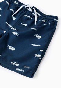 Pantaloni da bagno blu navy con motivo a pesce bianco, vita elasticizzata e cordoncino bianco. Il materiale ha una texture liscia e leggera.