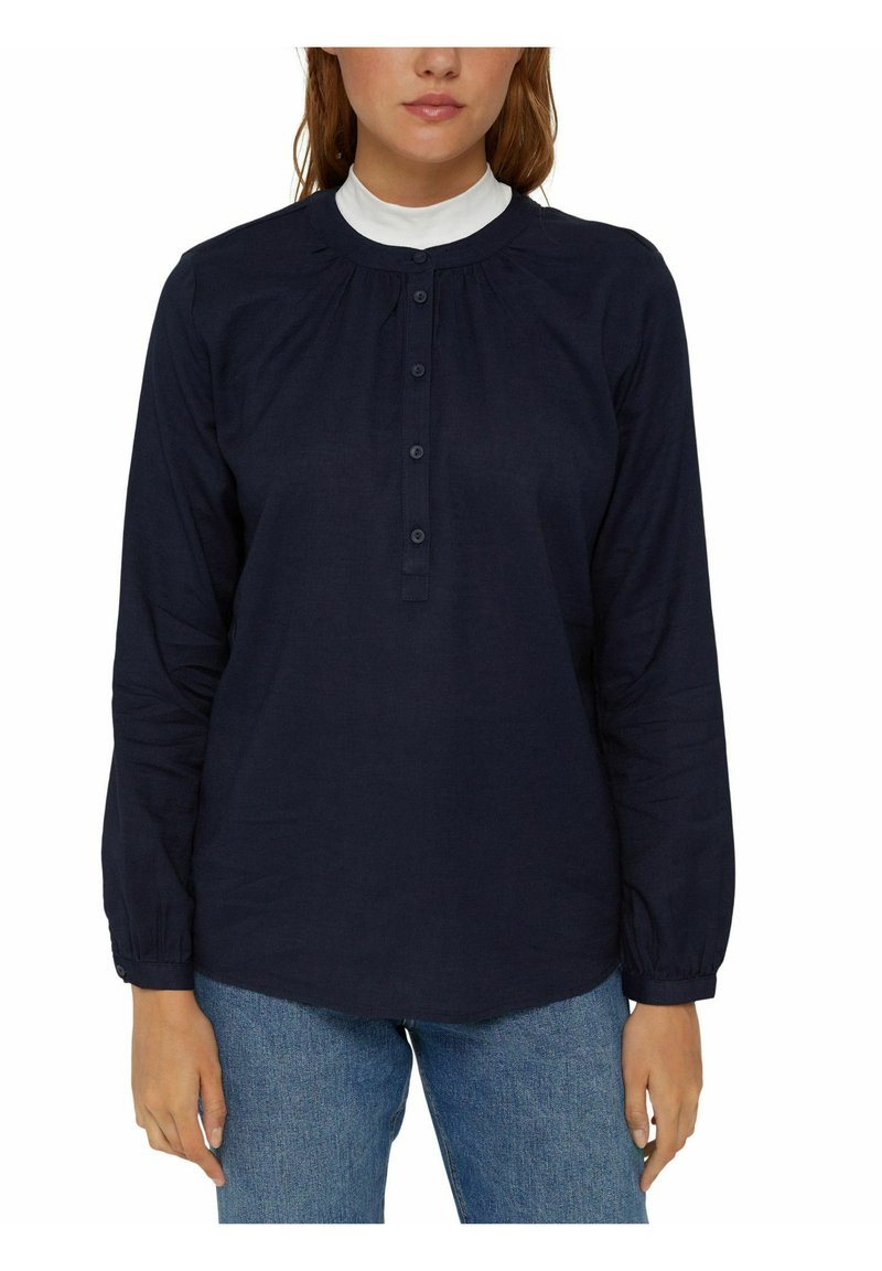 Marineblaues Langarmshirt mit Rundhals und Knopfleiste. Besitzt geraffte Details und taillierte Ärmel. Glatte Stofftextur.