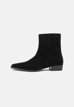 Schwarzer Wildleder-Stiefelette mit niedrigem Blockabsatz und spitzer Zehenpartie, seitlich auf einem einfarbigen hellen Hintergrund dargestellt.