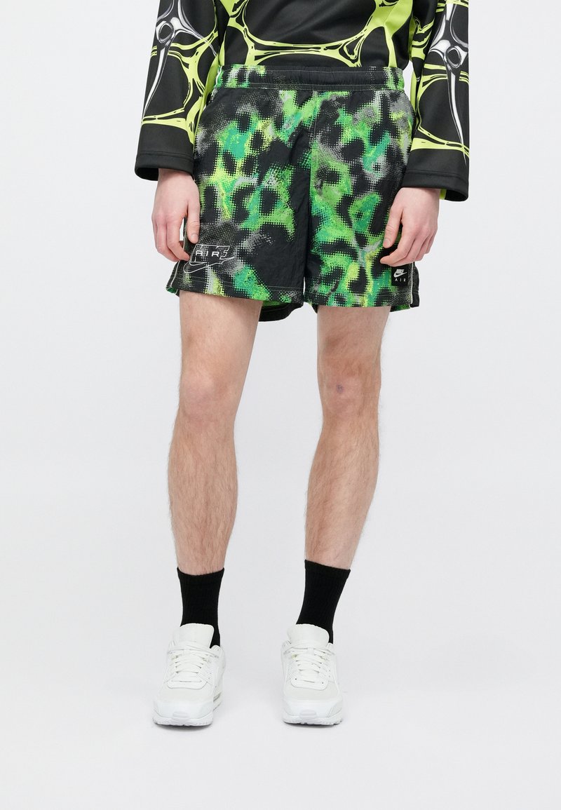 Black shorts with a green and grey abstract pattern, featuring an elastic waistband and side pockets, worn with white sneakers and black socks.