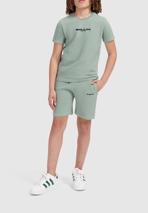 Groen gestructureerd set van een kortmouwshirt en shorts met het "BALLIN'" logo in het zwart, gecombineerd met witte sneakers met groene strepen.