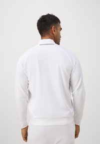Witte sweatshirt met een hoge kraag en geribde manchetten. Heeft een gladde, lichte textuur en een contrasterende slanke streep op de kraag.