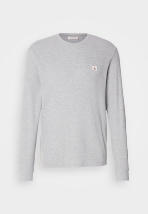 Light gray long-sleeve t-shirt made of cotton blend, featuring a round neckline and a small logo patch on the left chest.