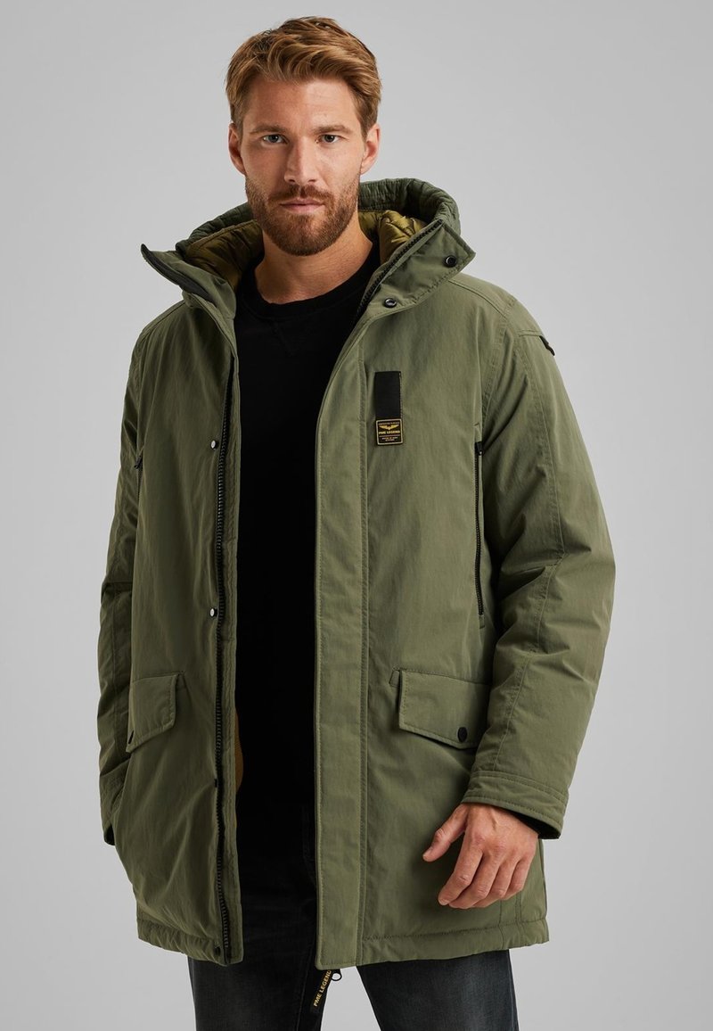 Groene parka jas met een rits en drukknoopsluiting, voorzien van een capuchon, twee voorkruiszakken en een stoffen label op de borst.
